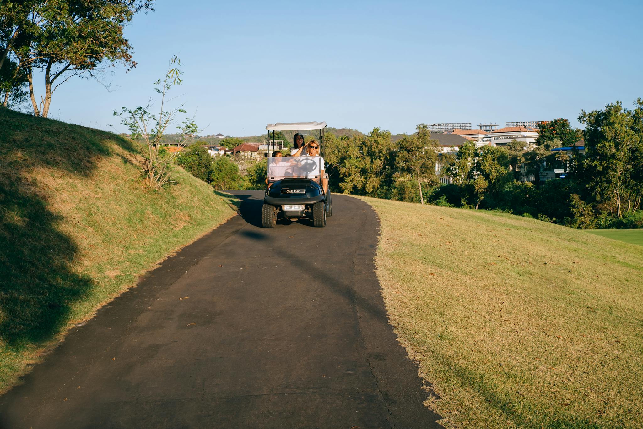 A family riding a golf cart along a scenic path on a sunny day, surrounded by greenery.