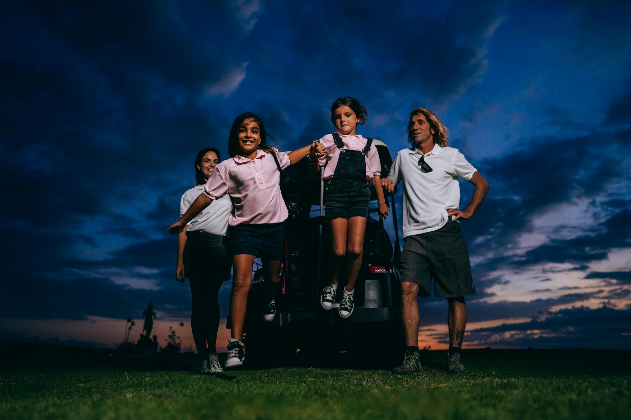 A happy family with kids having fun near a golf cart at sunset.