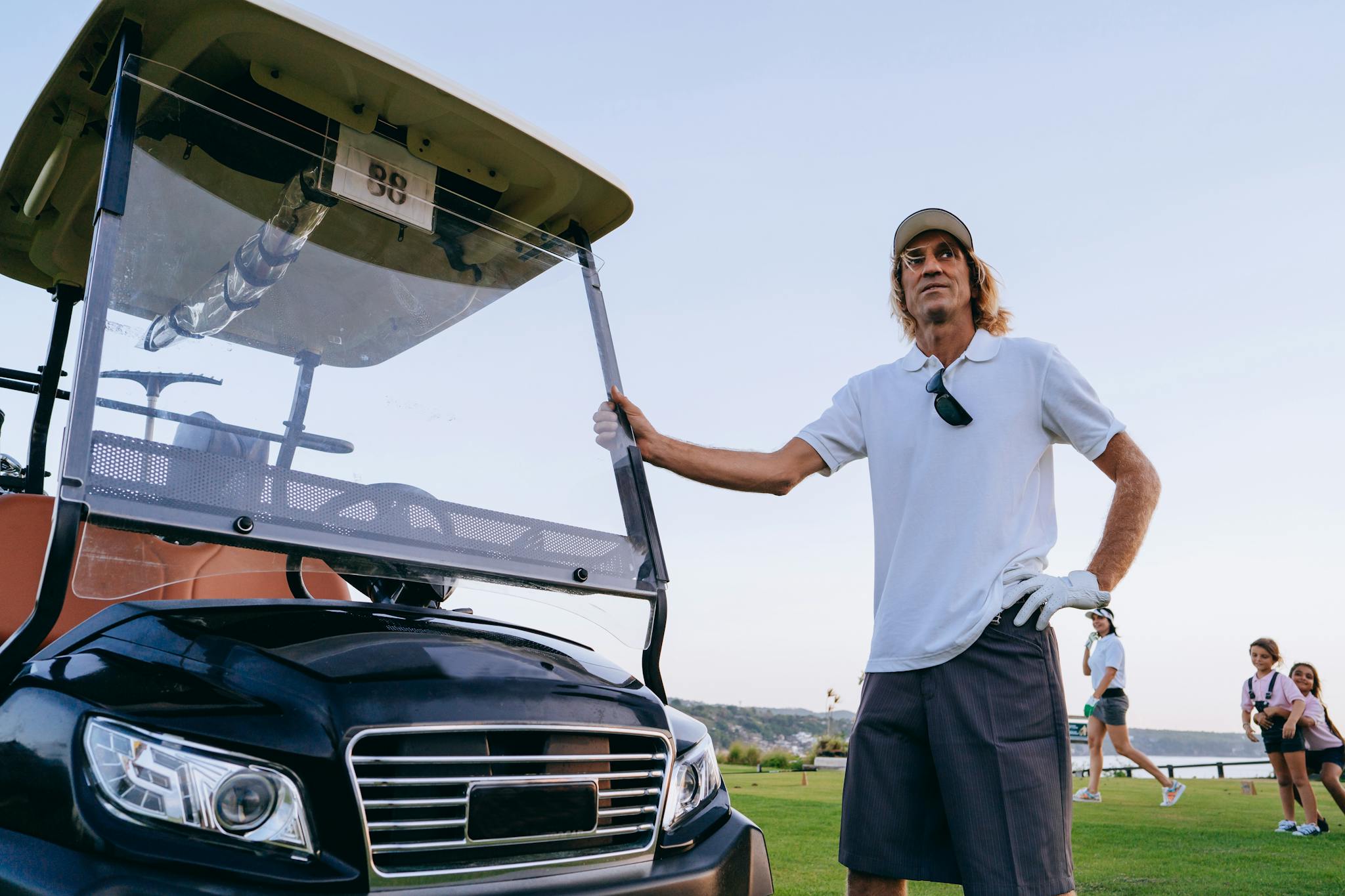 A man in casual golf attire stands confidently by a golf cart on the green.