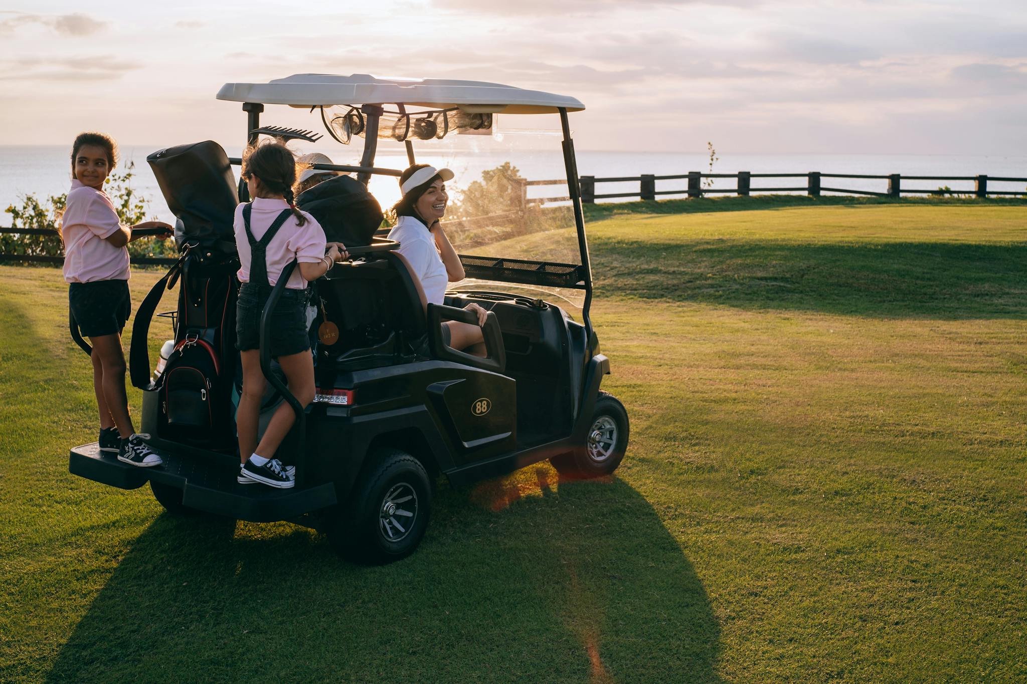 Cheerful family with children riding a golf cart outdoors during a scenic sunset at a golf course.