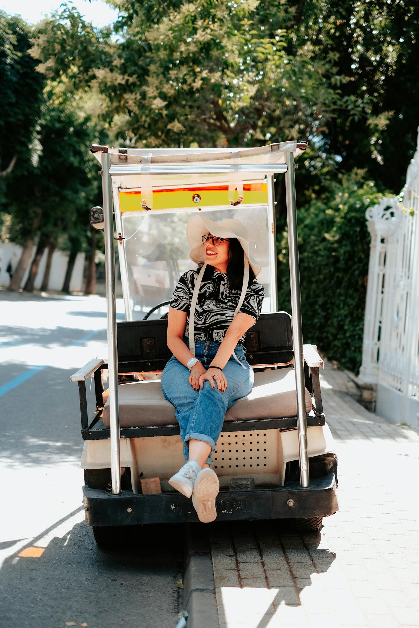 Woman sitting on a golf cart enjoying a sunny day, wearing a stylish sun hat.